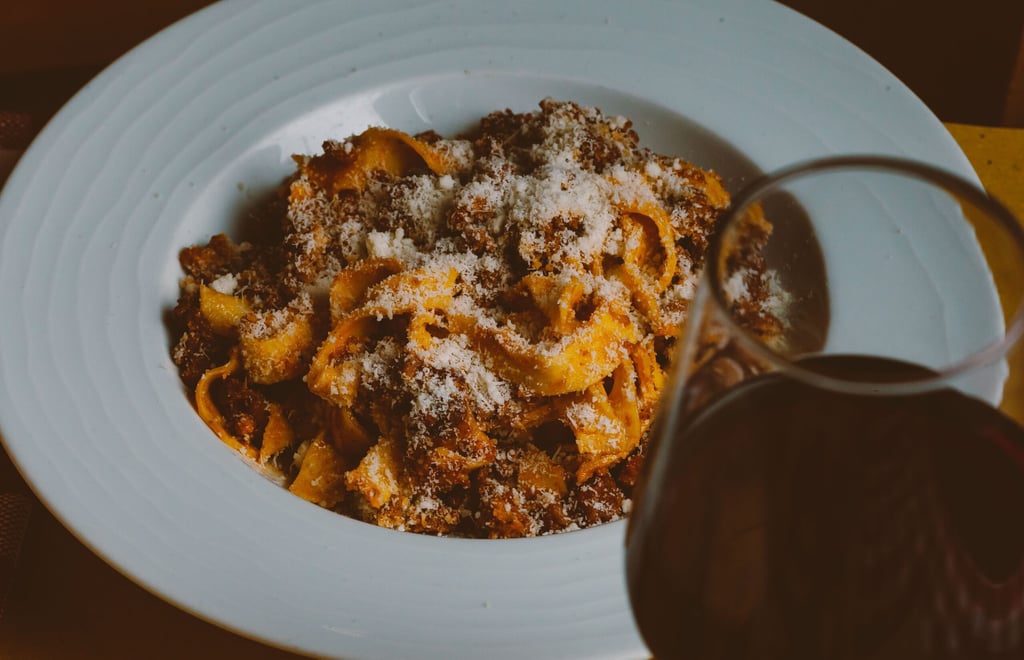 A macaroni with Bolognese sauce and grated fresh Parmesan cheese in white plate and glass of wine