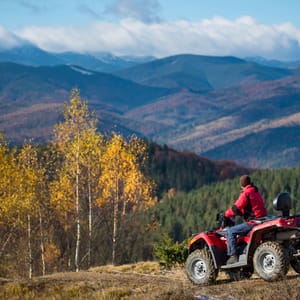 Male on an ATV on the hilly road enjoying mountains, automn forest and blue sky. The concept of an active holiday in the mountains