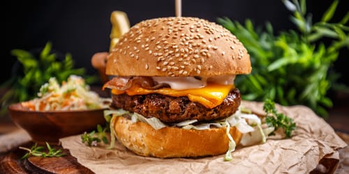 Tasty grilled beef burger with cheese and cabbage served on pieces of brown paper
